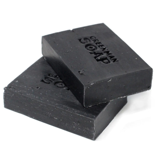 Dos pastillas de jabón rectangulares de color negro intenso, apiladas, con letras grabadas en su superficie.