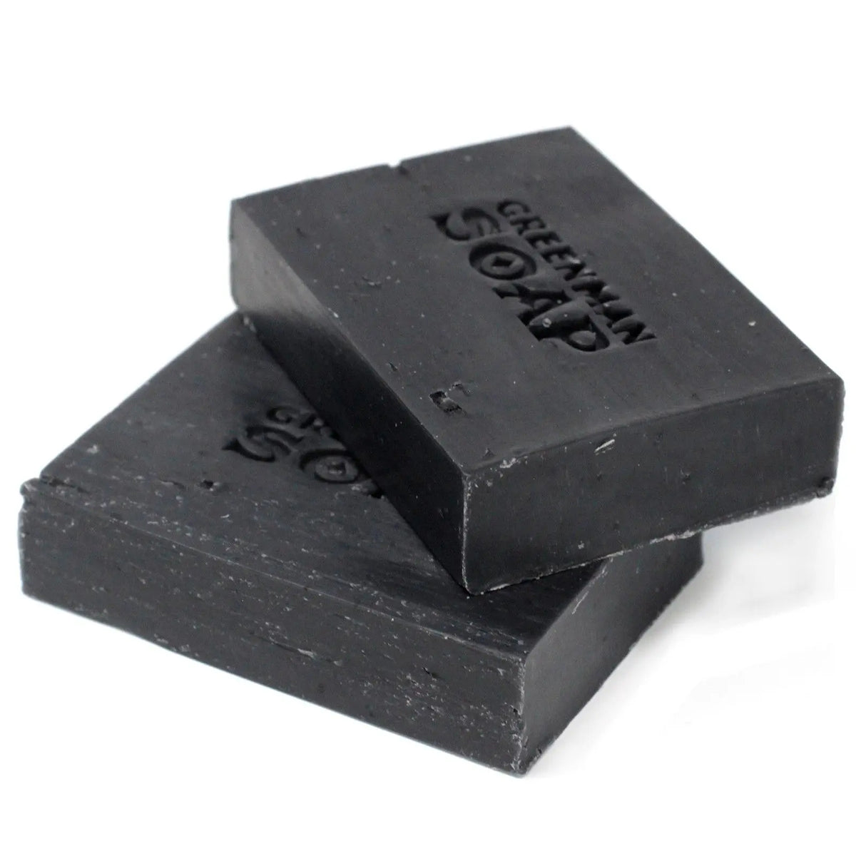 Dos pastillas de jabón rectangulares de color negro intenso, apiladas, con letras grabadas en su superficie.