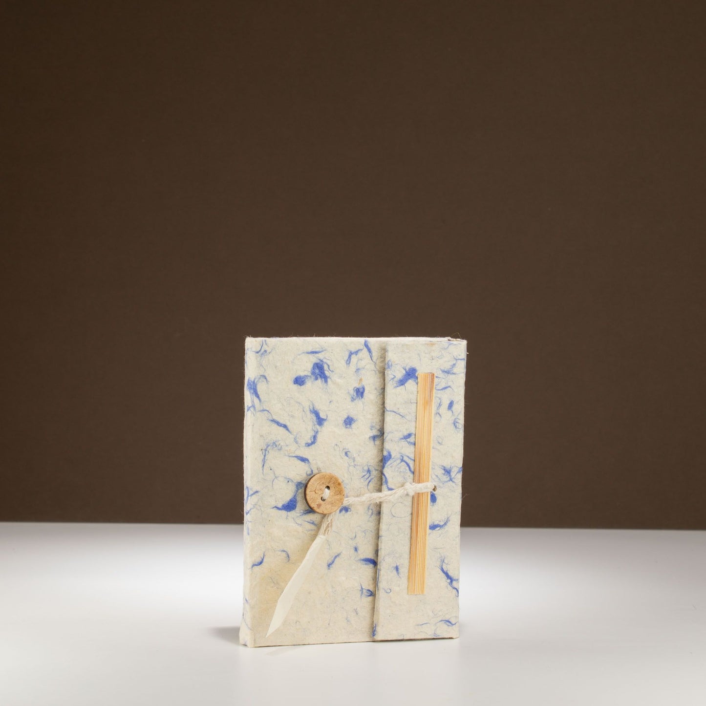 Cuaderno artesanal en papel reciclado blanco y azul, con cierre de cuerda y botón de madera. Ideal para notas.