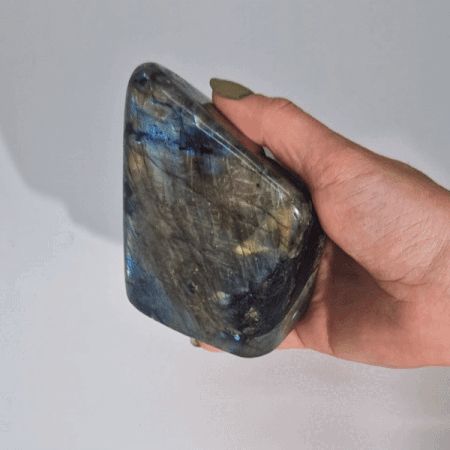 Piedra de labradorita gris con destellos azules, pulida y con forma irregular, ideal para coleccionistas y decoración.