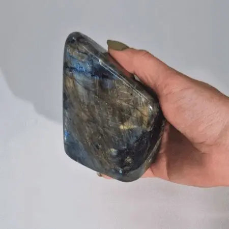Piedra de labradorita gris con destellos azules, pulida y con forma irregular, ideal para coleccionistas y decoración.