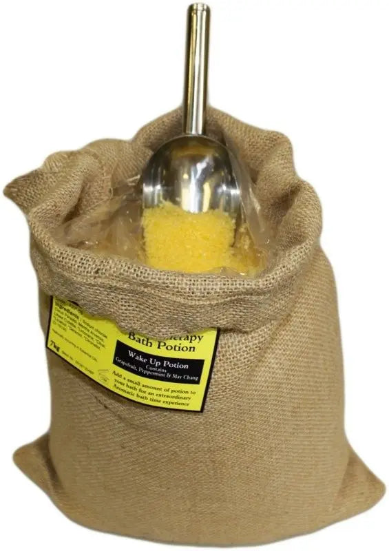 Saco de yute con 7kg de sales de baño amarillas estimulantes y pala de metal, marca Ancient Wisdom. Fondo blanco.