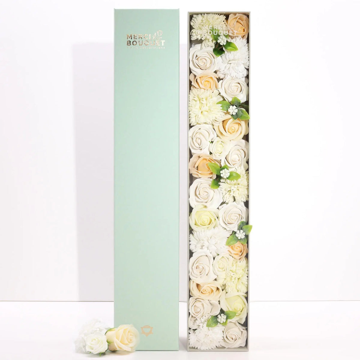 Caja rectangular alta con flores de jabón en tonos blanco y marfil, acompañada de su tapa verde agua a un lado.