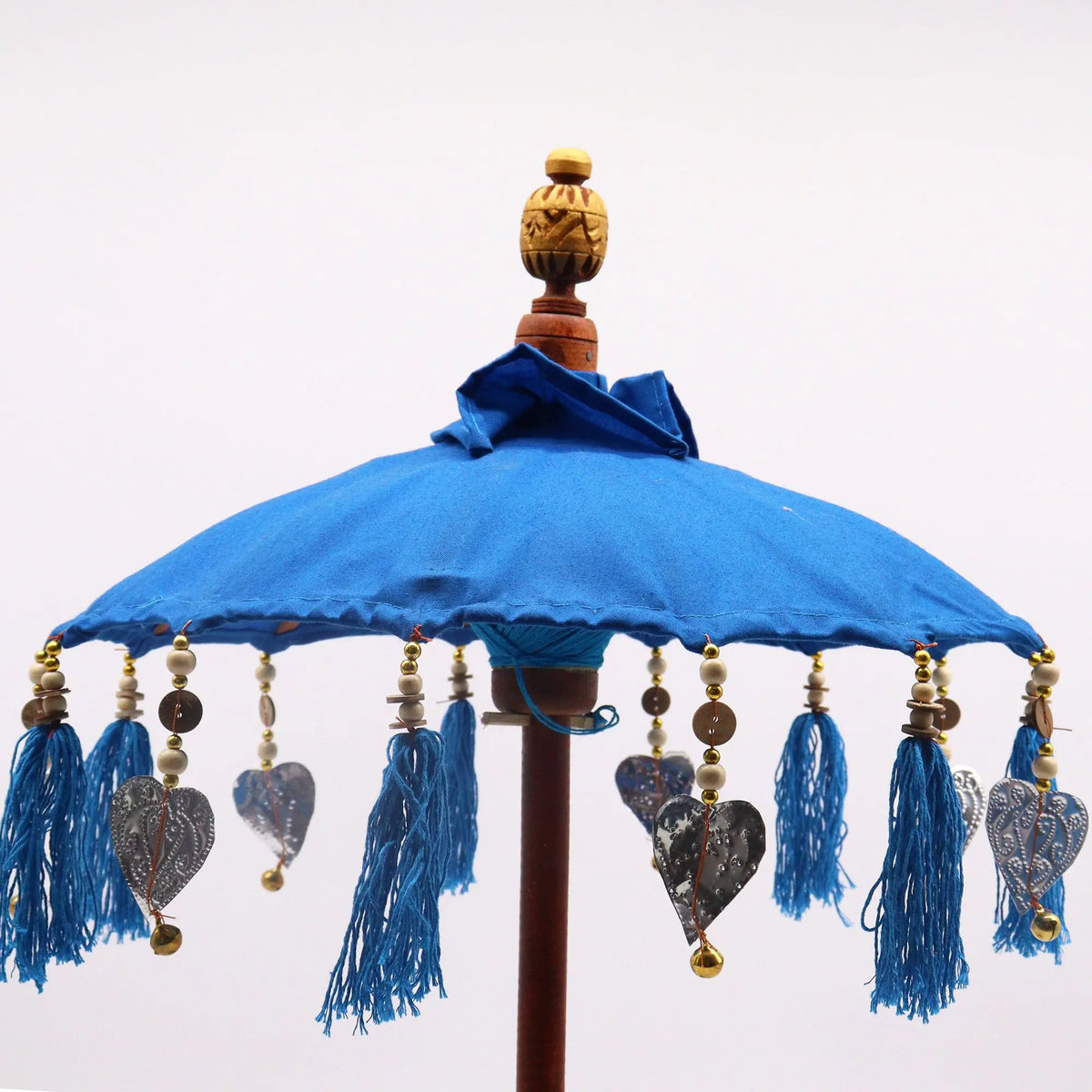 Sombrilla artesanal de algodón turquesa con borlas, cuentas de madera y colgantes metálicos en forma de corazón.