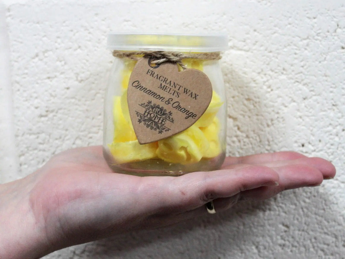 Frasco de vidrio pequeño con trozos de cera amarilla, tapa transparente y etiqueta de papel en forma de corazón.