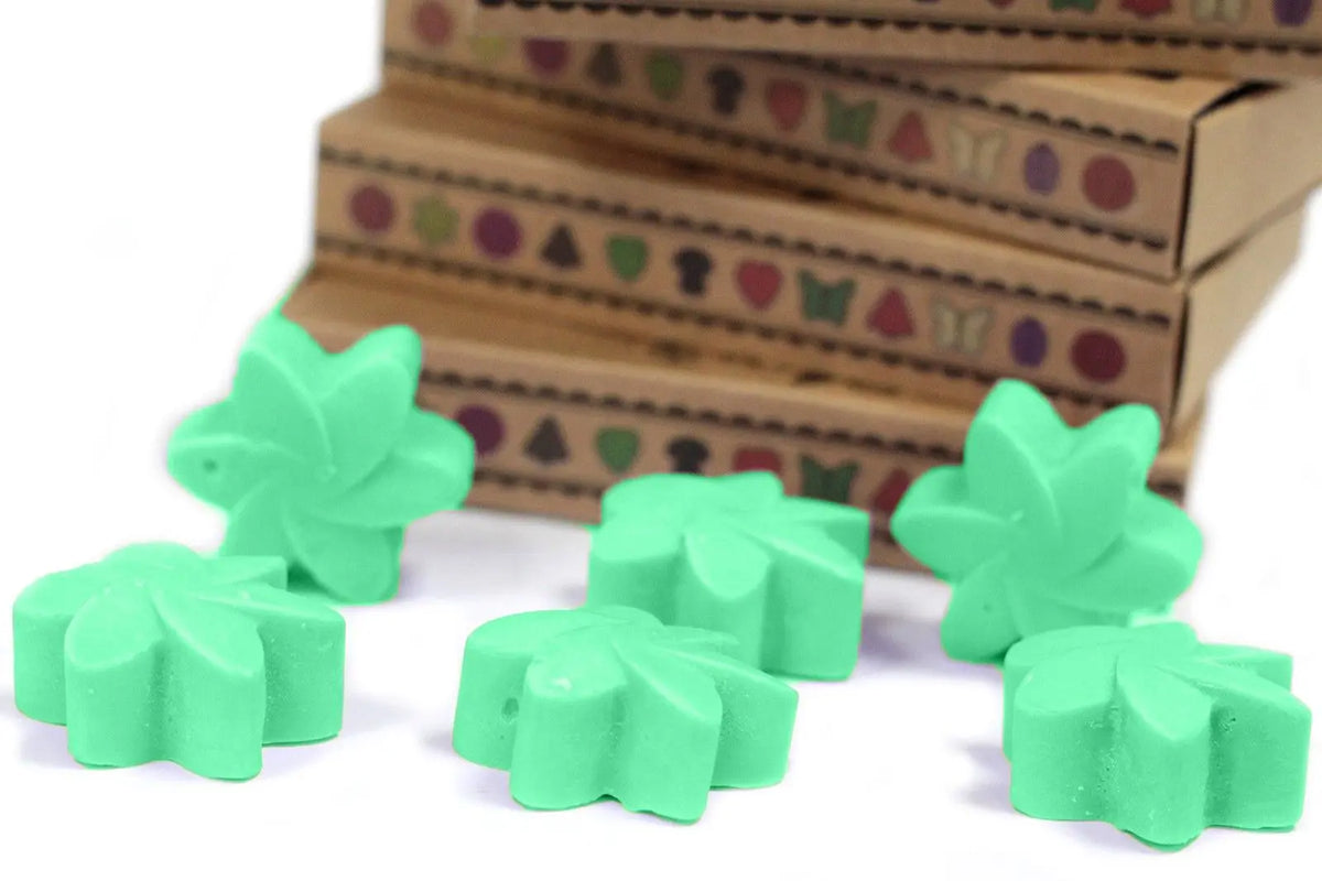 Seis piezas de cera de soja verde con forma de flor frente a cajas de regalo de cartón apiladas.