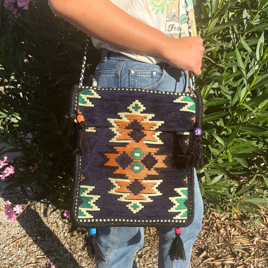 Bolso bandolera de estilo kilim azul marino, con patrón geométrico, borlas decorativas y asa trenzada.