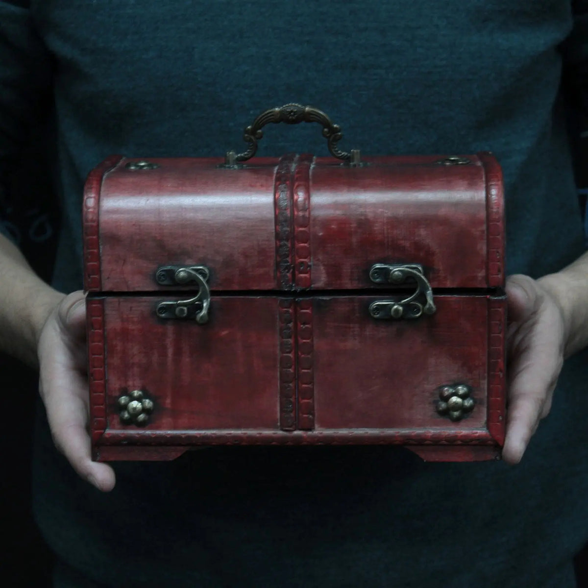 Caja de madera roja vintage con herrajes metálicos, estilo retro y asas decorativas.