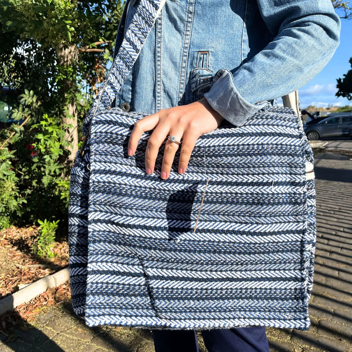 Bolso para portátil de tela tejida con rayas azules y blancas, diseño rectangular con correa larga, estilo artesanal.