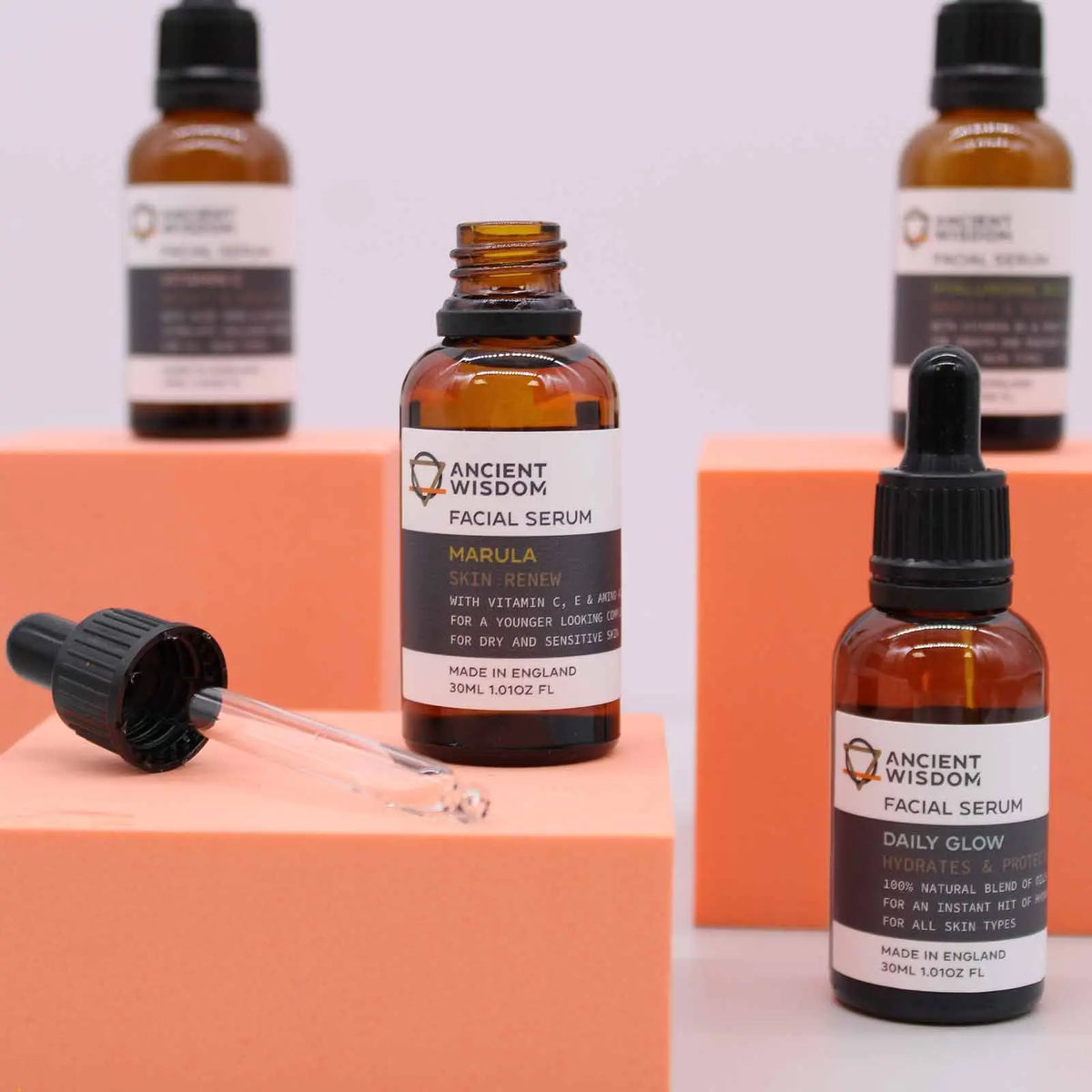 Frascos de vidrio ámbar con cuentagotas de la marca Ancient Wisdom sobre pedestales cuadrados de color naranja.