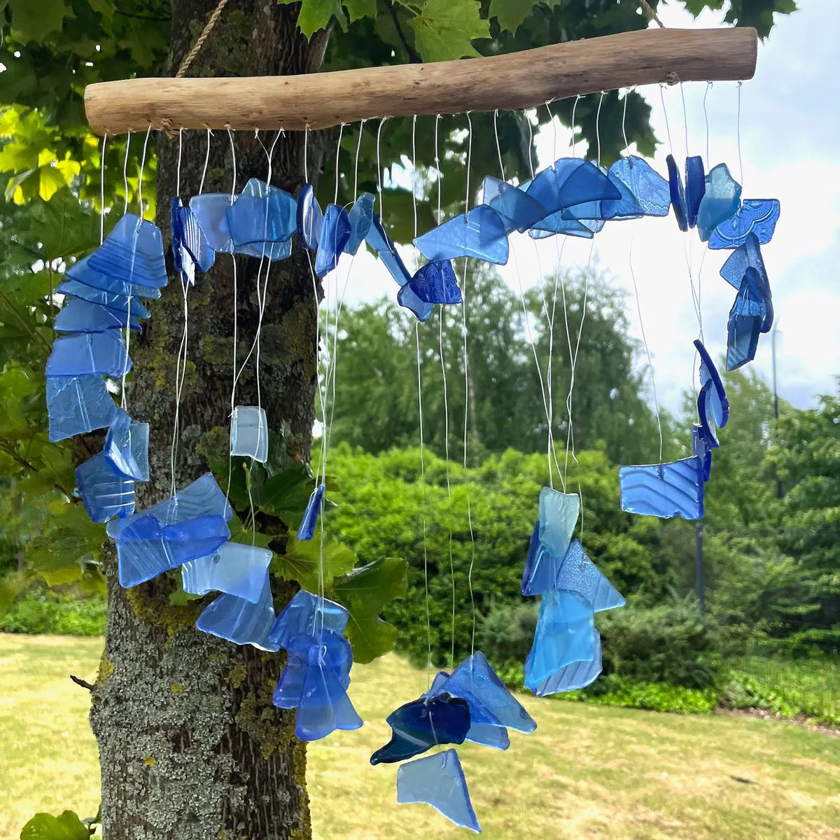 Carillón decorativo de piezas de vidrio reciclado azul y blanco, colgado de una rama rústica en forma de corazón.