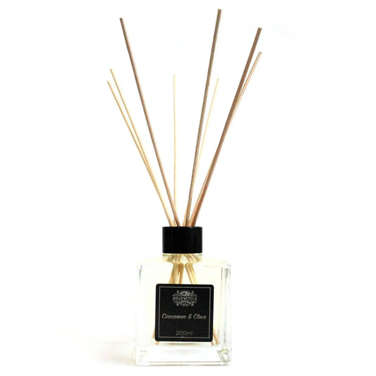 Difusor de varillas con frasco de cristal cuadrado, tapa negra y etiqueta de canela y clavo sobre fondo blanco.
