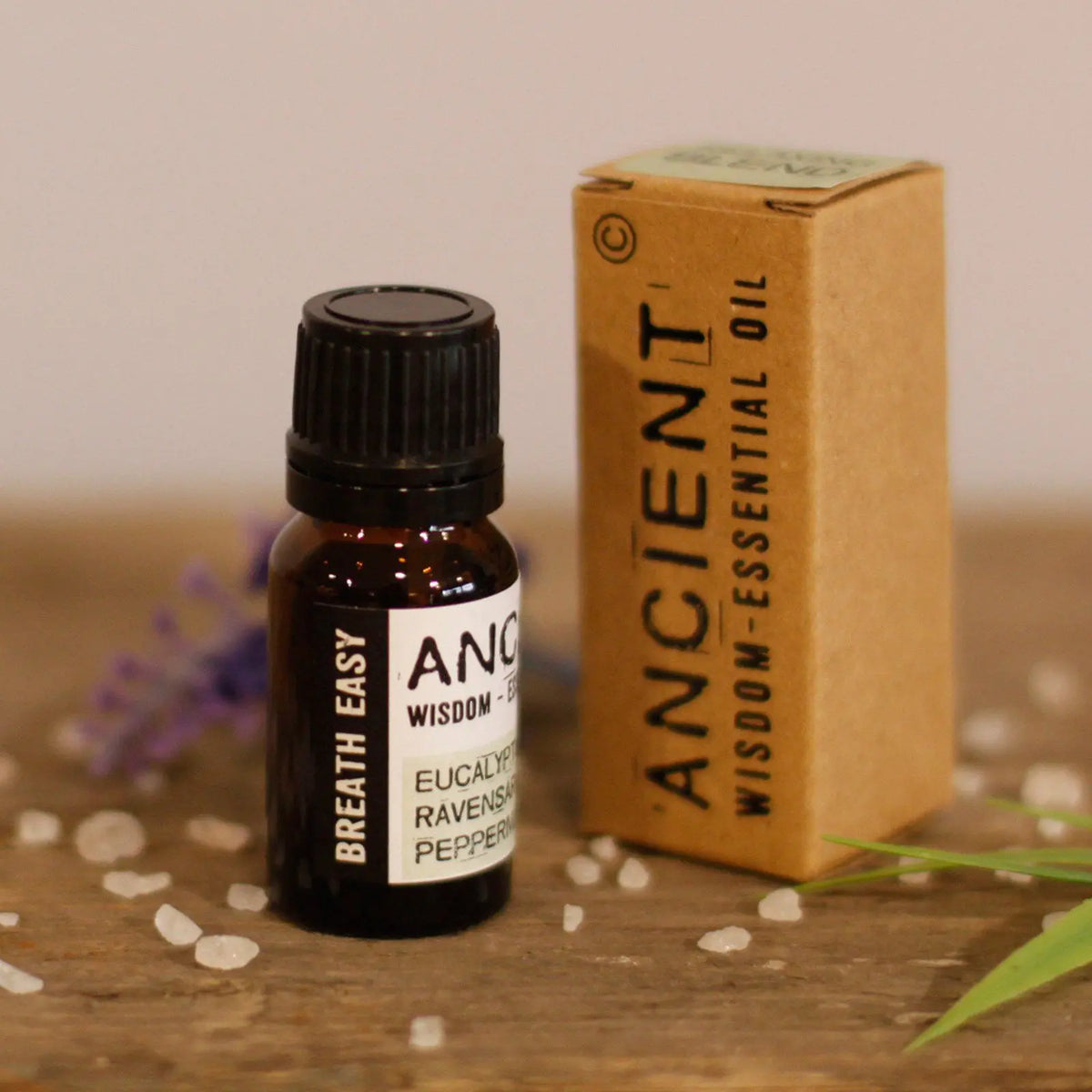 Frasco de aceite esencial de 10ml junto a su caja de cartón kraft, sobre superficie de madera con detalles decorativos.