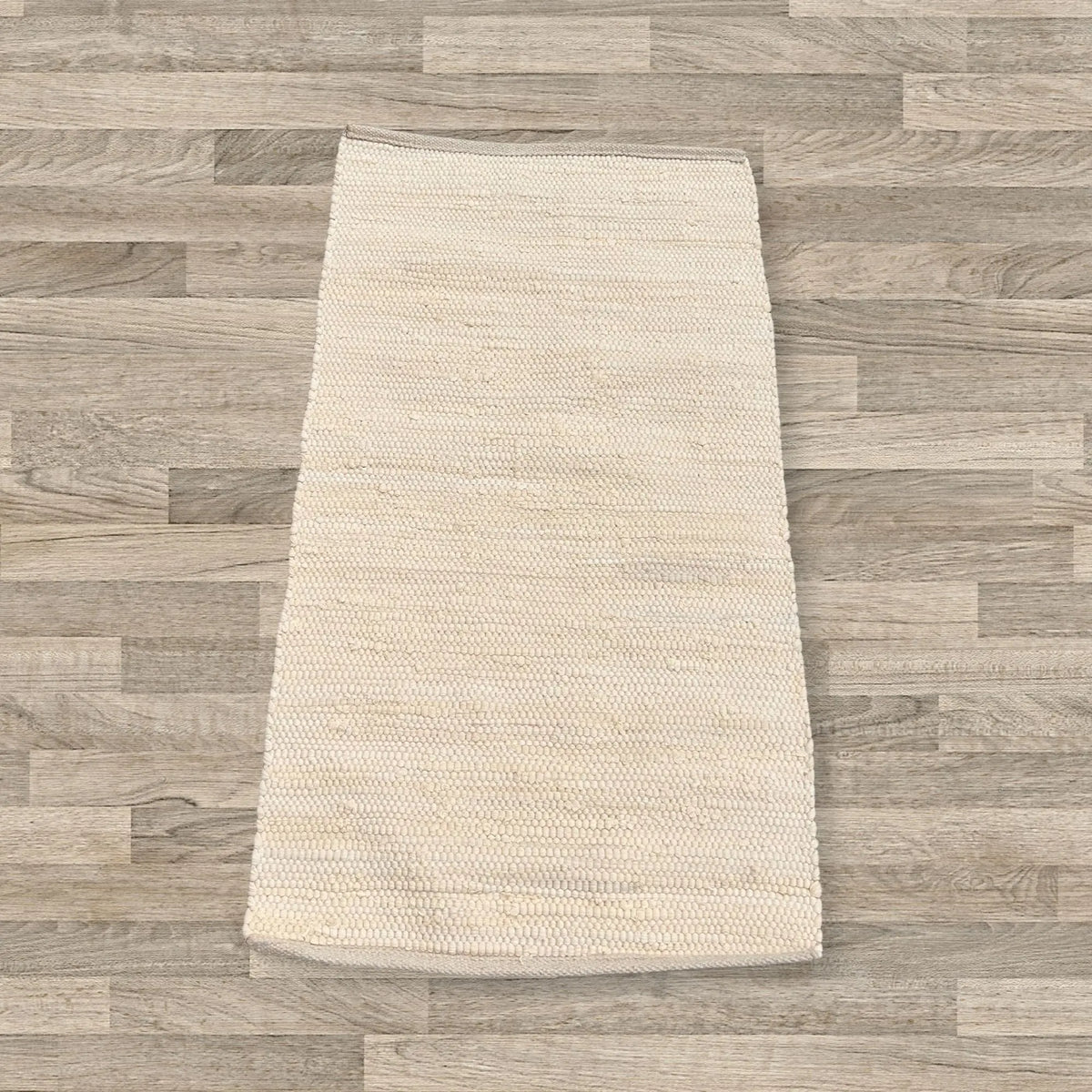Alfombra rectangular de algodón color crema, tejida a mano con textura de cuentas, sobre suelo de madera.