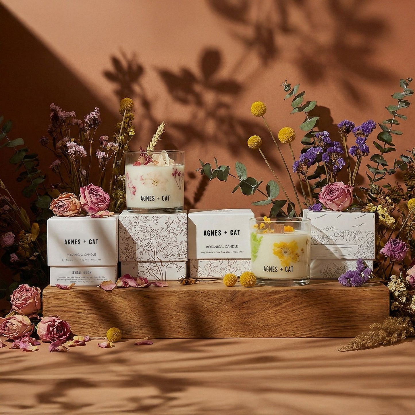 Velas aromáticas en frascos de vidrio con flores secas, tonos amarillos y rosas, sobre madera y decoradas con flores.