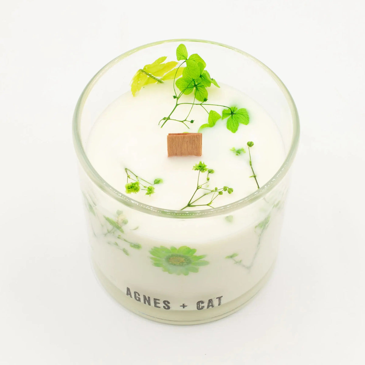 Vela decorativa blanca en frasco de vidrio con flores verdes y tapa de madera, estilo elegante y natural.