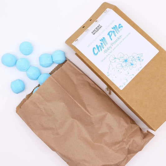Mini bombas de baño efervescentes de color azul saliendo de una bolsa de papel kraft junto a su caja de presentación.