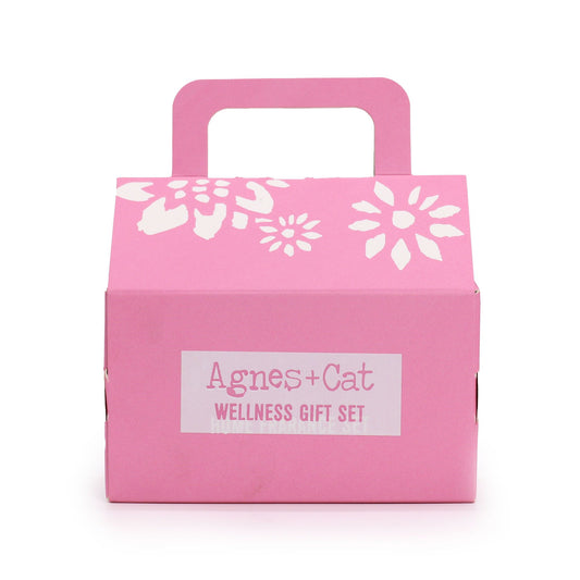 Caja de regalo rosa con asa, diseño floral blanco y etiqueta "Agnes & Cat Wellness Gift Set" al frente.