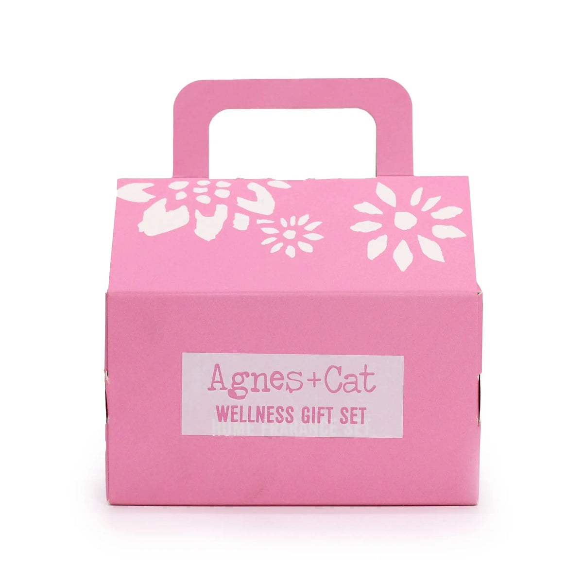 Caja de regalo rosa con asa, diseño floral blanco y etiqueta "Agnes & Cat Wellness Gift Set" al frente.