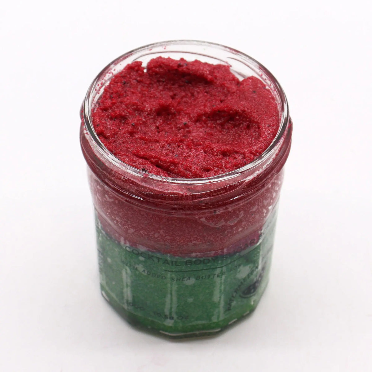 Frasco de vidrio con exfoliante corporal de azúcar rojo brillante y textura granular sobre fondo blanco.