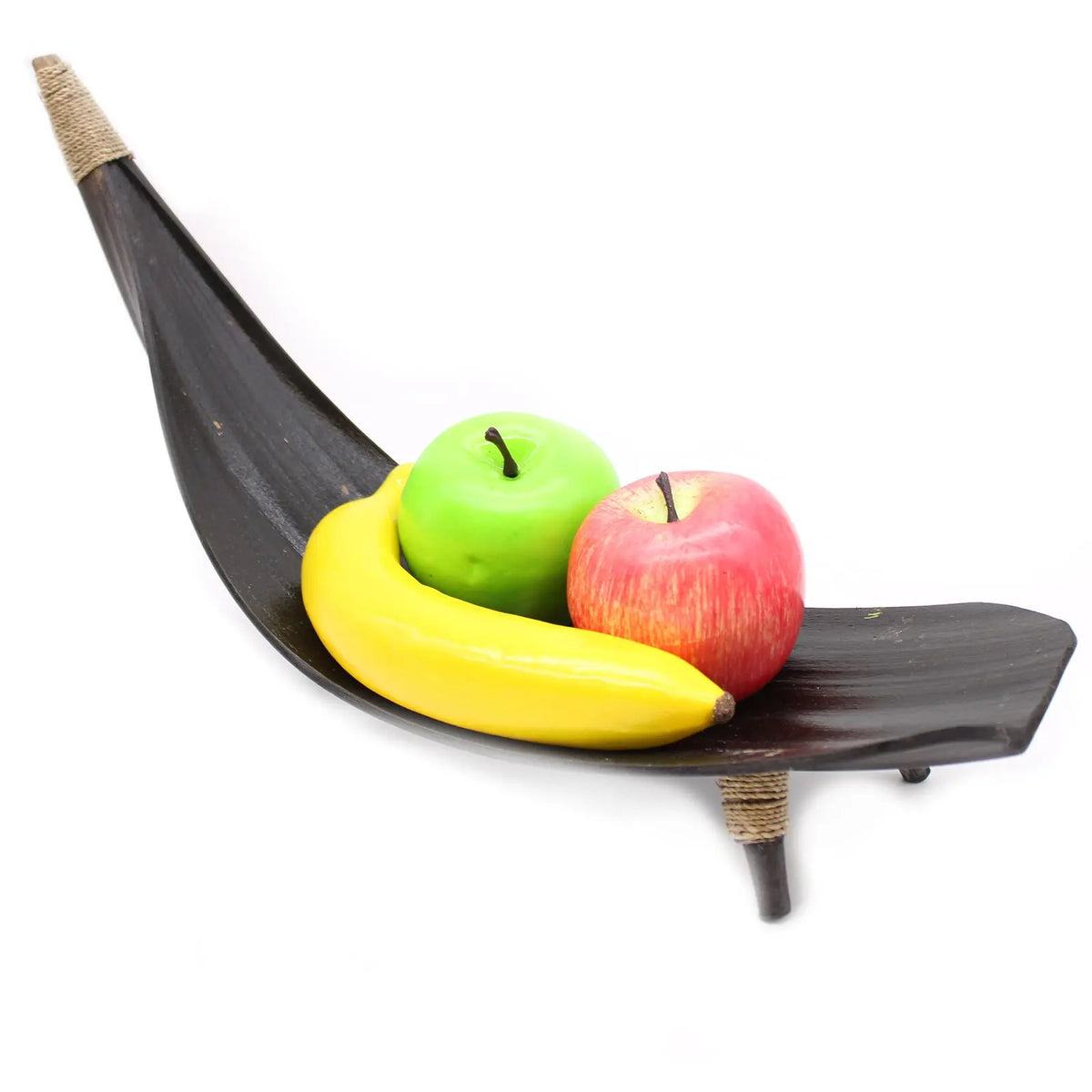 Frutero de hoja de coco color chocolate con forma de barca, con un plátano, una manzana verde y una roja dentro.