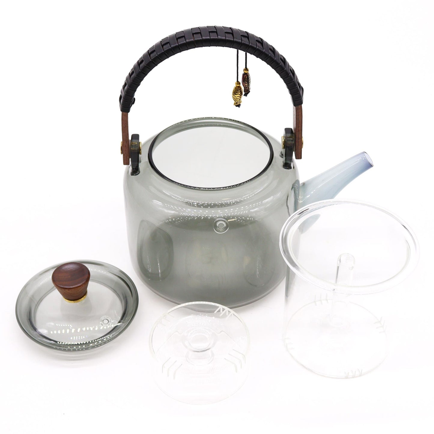 Tetera de vidrio gris con infusor, tapa con pomo de madera y asa curva decorada con colgantes, sobre fondo blanco.