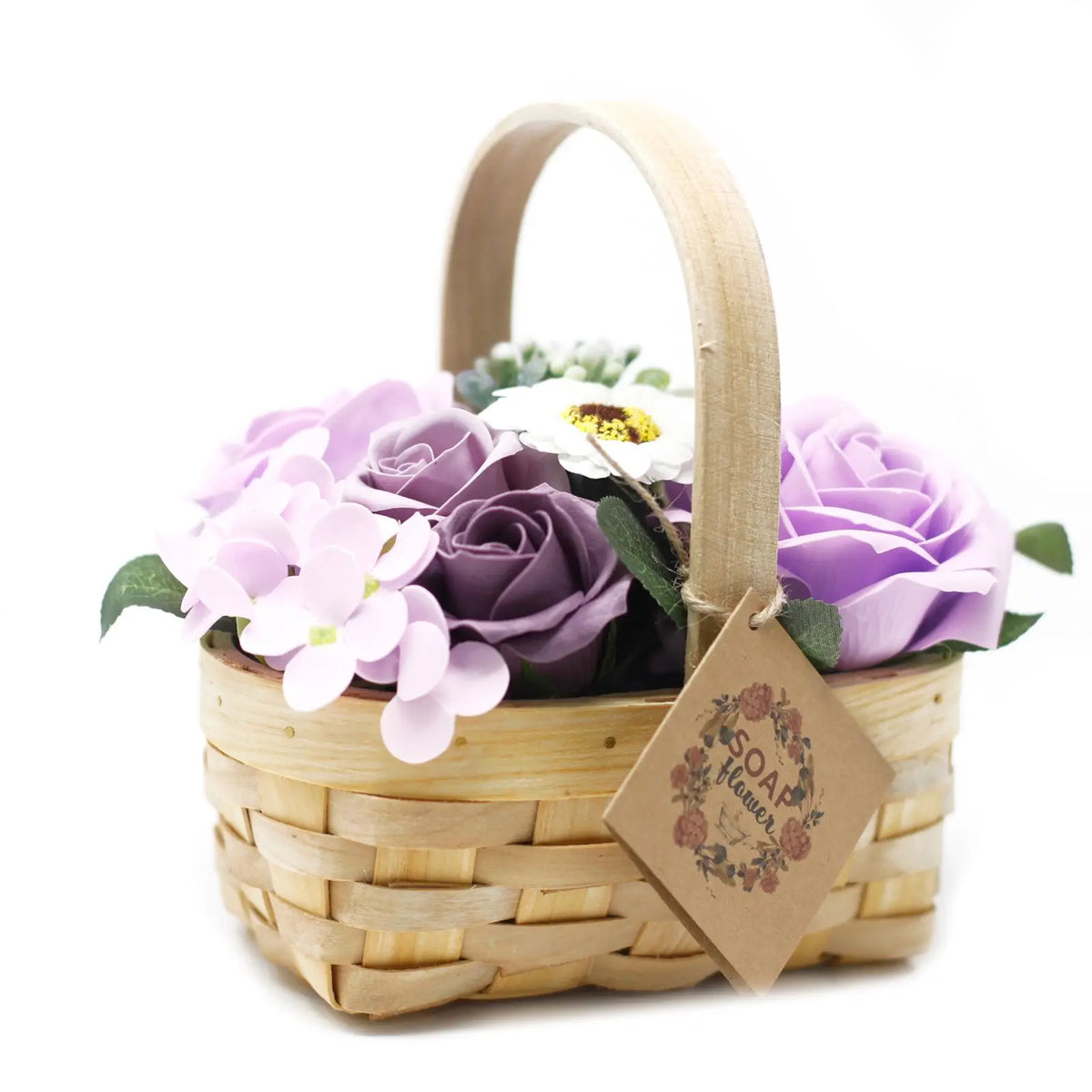 Canasta de mimbre con rosas y flores de jabón en tonos lilas y violetas, con etiqueta decorativa.