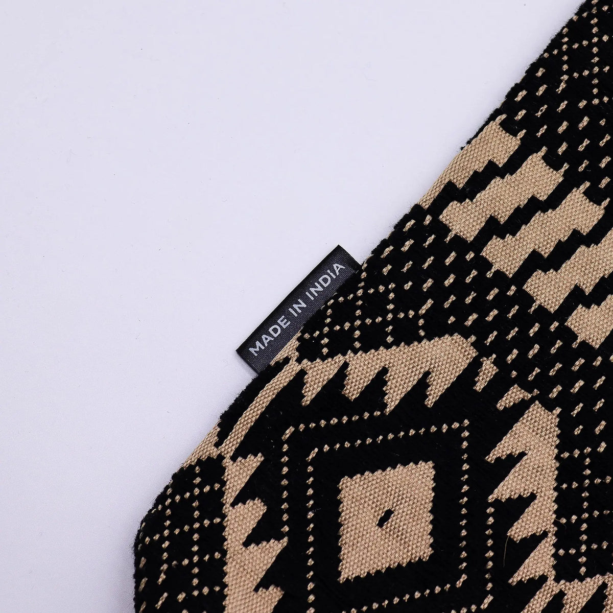 Alfombrilla decorativa de algodón en tonos negro y beige con diseño geométrico, hecha en India.