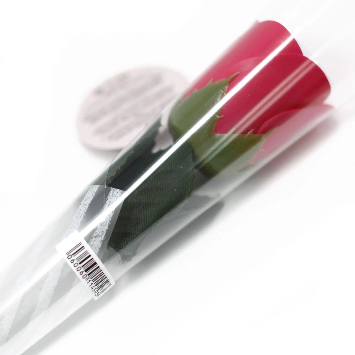 Flor de jabón roja con tallo verde, envuelta en plástico transparente. Regalo decorativo elegante sobre fondo blanco.