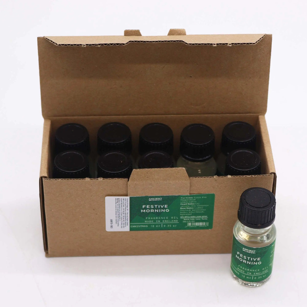 Caja de cartón con 10 frascos de aceite de 10ml, tapa negra y etiqueta verde con nombre "Festive Morning". Fondo blanco.