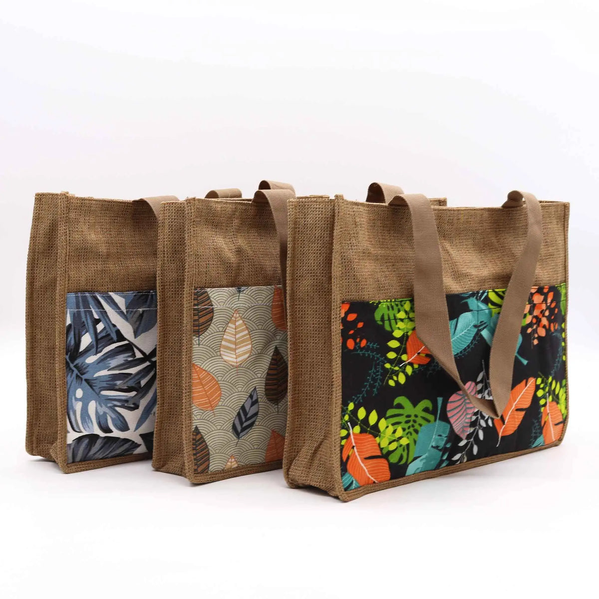 Tres bolsas de compra rectangulares de yute natural con bolsillos frontales estampados en distintos diseños botánicos.