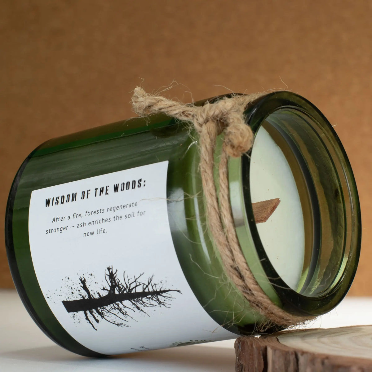 Vela verde en frasco de vidrio con etiqueta "Wisdom of the Woods" y cuerda y tapa de madera. Aromas terrosos.