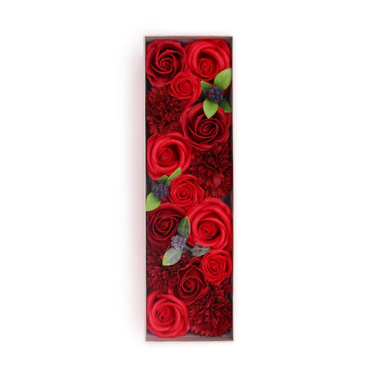 Caja rectangular larga con rosas y claveles rojos de jabón decorados con pequeñas hojas verdes y bayas oscuras.