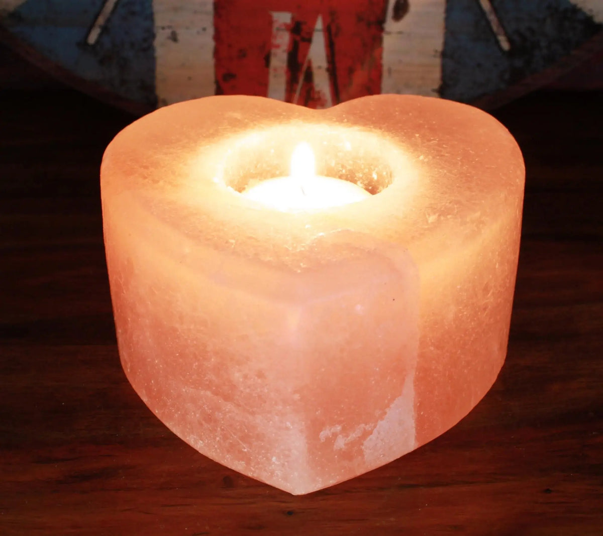 Soporte de vela en forma de corazón de sal del Himalaya, color naranja suave con una vela encendida en el centro.