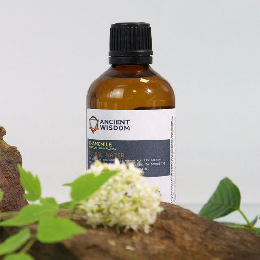 Frasco de vidrio ámbar con hidrolato de manzanilla sobre una superficie rústica con flores y hojas verdes de fondo neutro