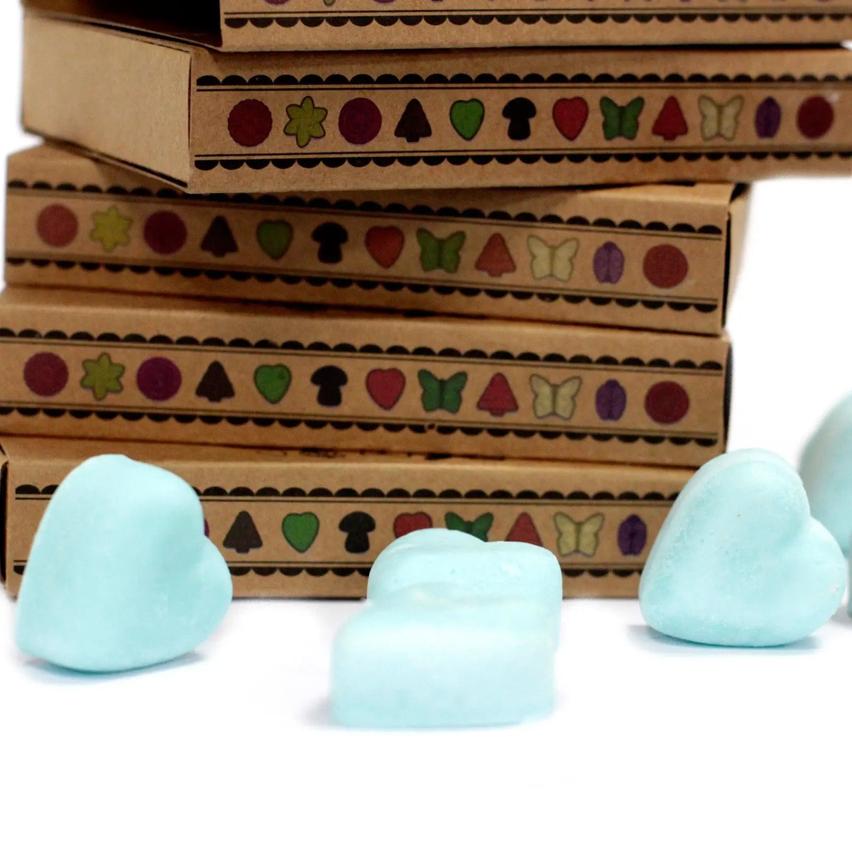 Cajas de cartón kraft apiladas con diseños de figuras coloridas junto a tres ceras de soja en forma de corazón azul.