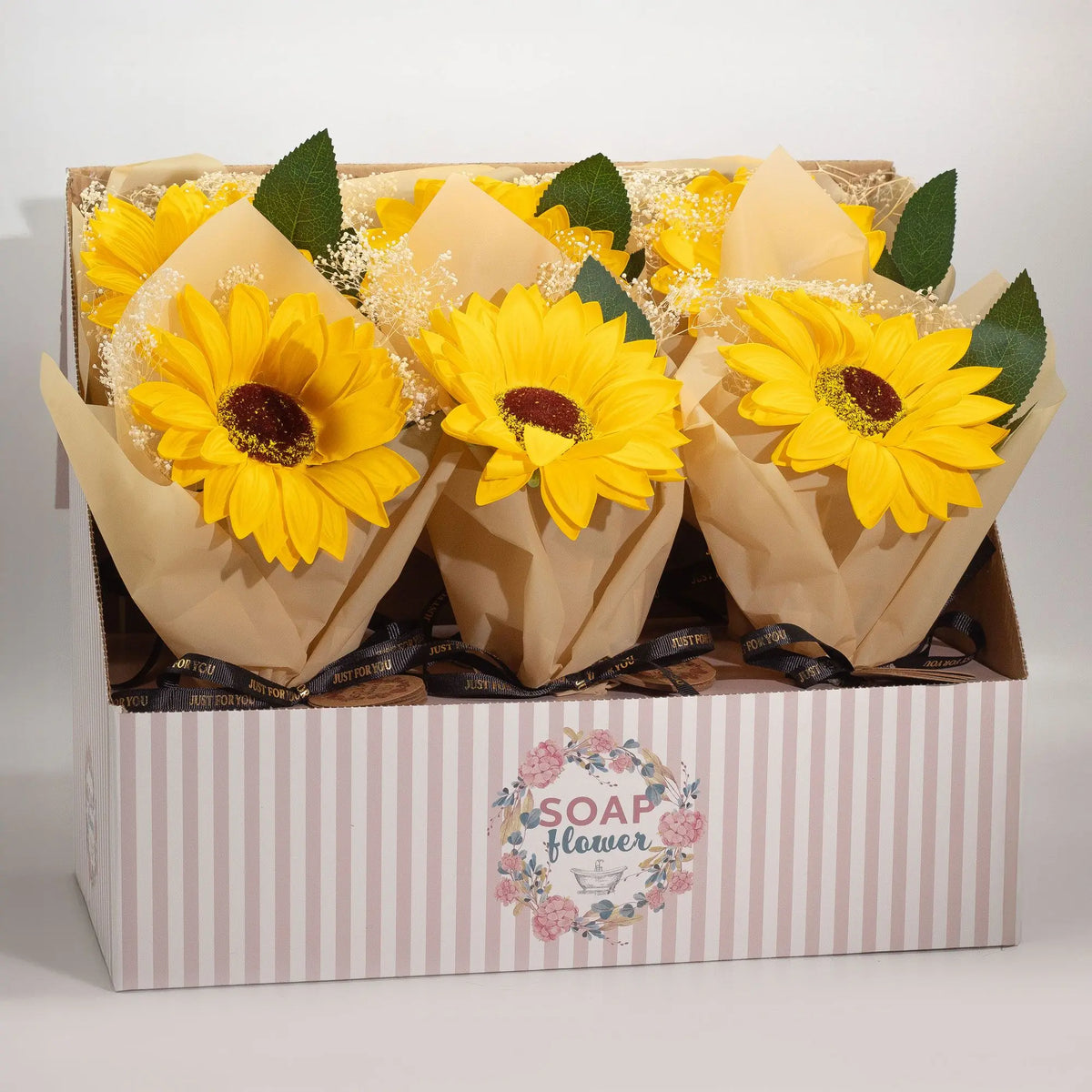 Expositor con ramos de girasoles de jabón amarillos, envueltos en papel craft con detalles de flores blancas y cinta.