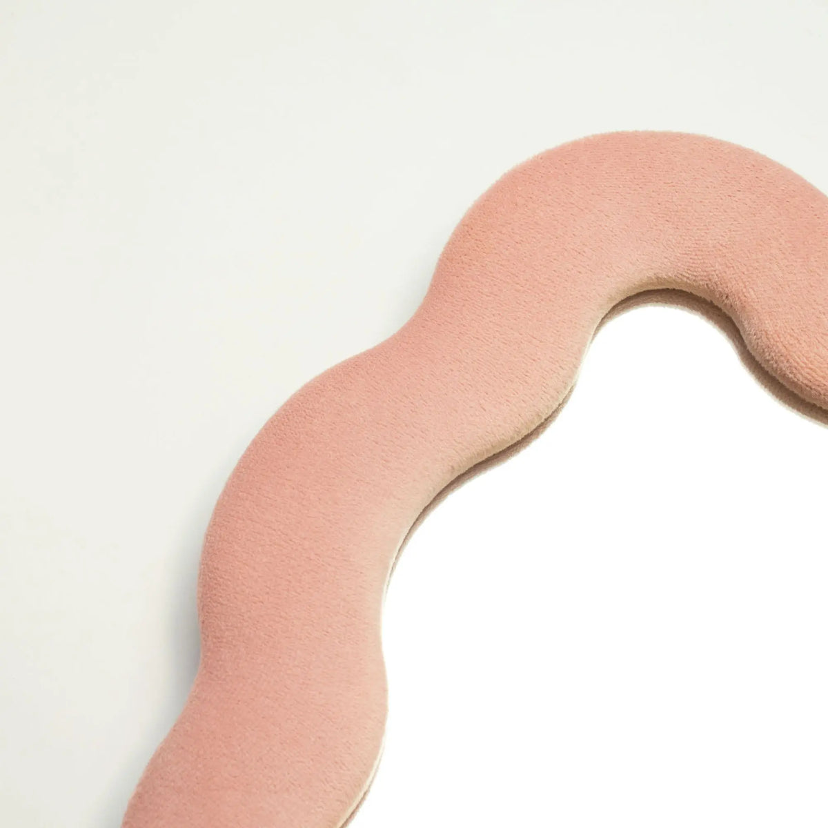 Espejo de forma ondulada con borde de terciopelo rosa y fondo blanco, ideal para decoración moderna.