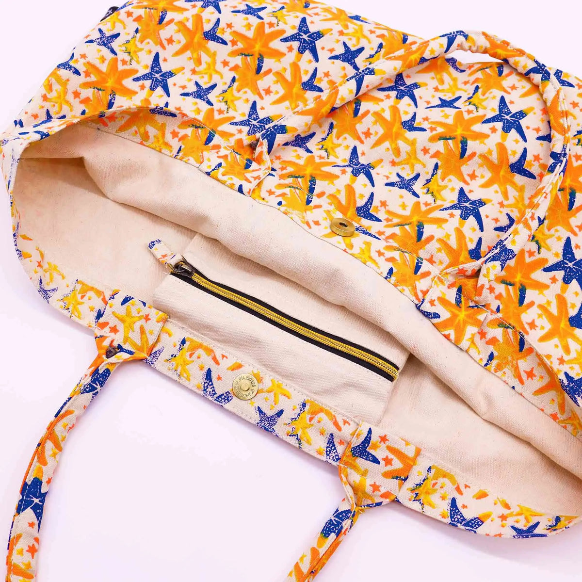 Bolso tote de tela color crema con estampado de estrellas de mar naranjas y azules, cierre de botón y bolsillo interno