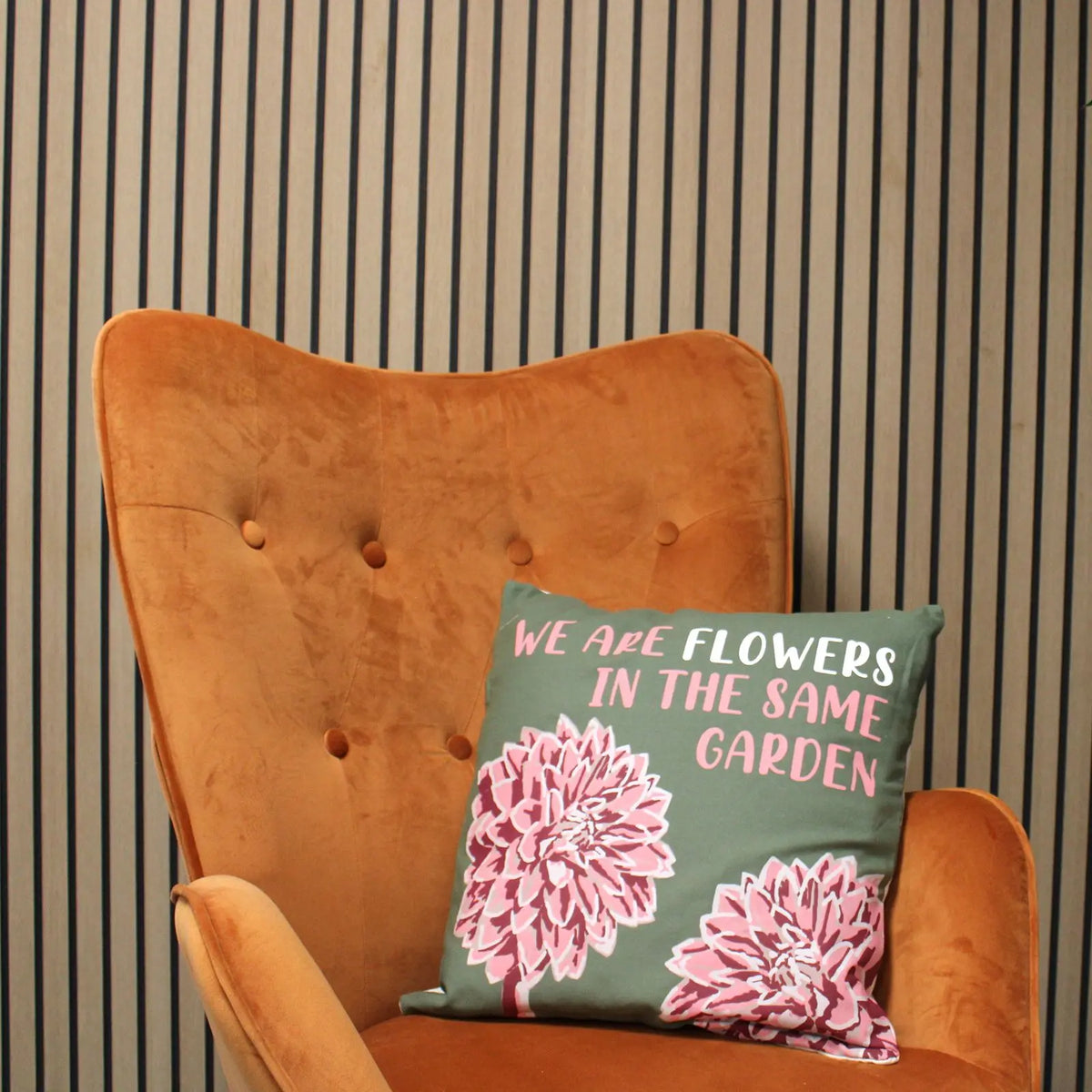 Funda de cojín de algodón verde con estampado de flores rosas y frase motivadora sobre un sillón de terciopelo naranja