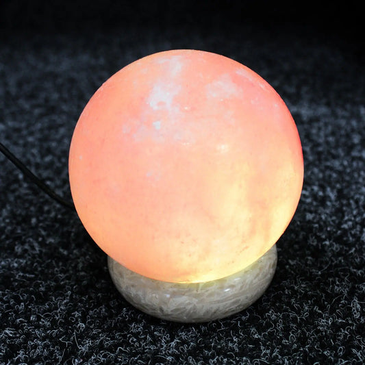 Lámpara de sal del Himalaya esférica de 8 cm con luz naranja cálida sobre base circular de piedra, conectada por USB.