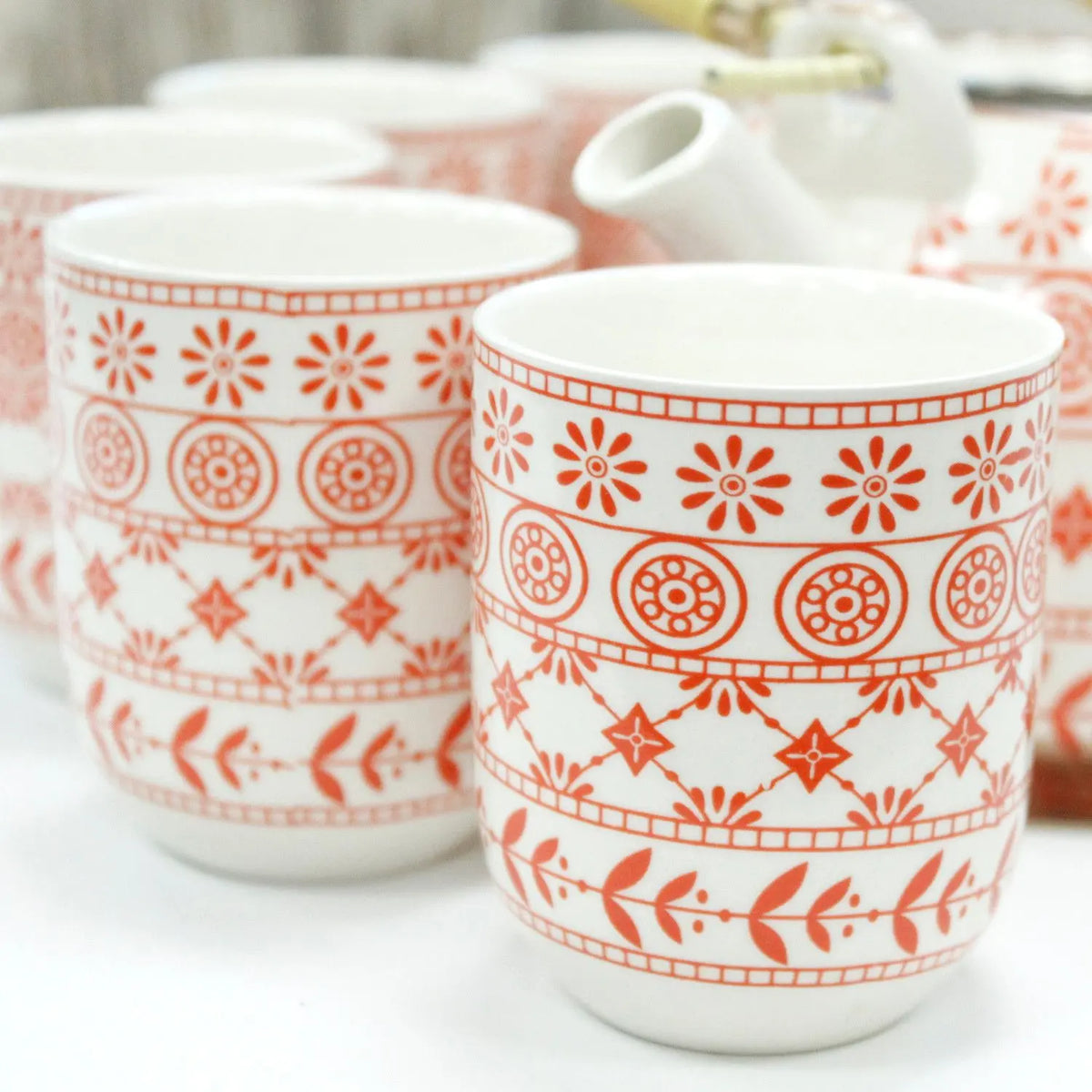 Set de tetera y tazas de cerámica blanca con estampado floral y geométrico en color naranja.