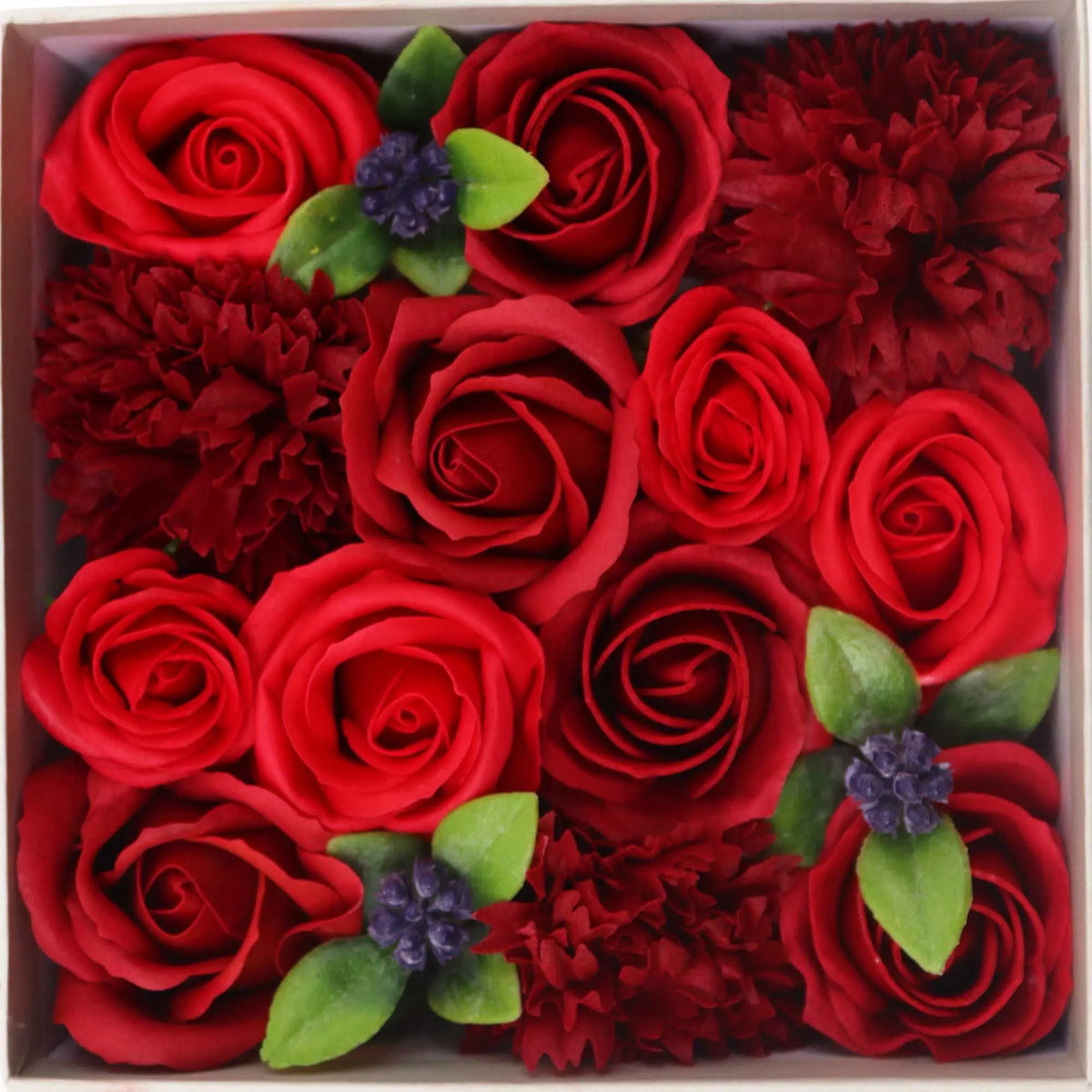 Caja cuadrada con rosas y flores de jabón rojas realistas, acompañadas de pequeñas hojas verdes y detalles decorativos