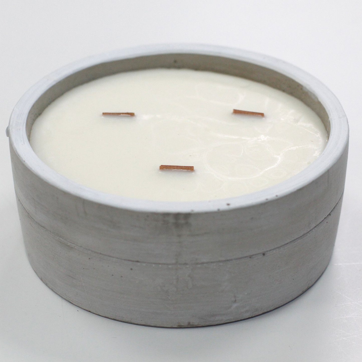 Vela redonda de cera blanca con tres pabilos de madera en un recipiente de hormigón gris de estilo minimalista industrial