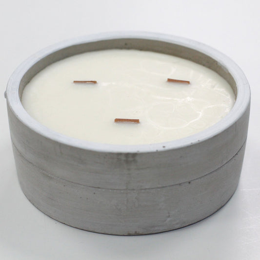 Vela redonda de cera blanca con tres pabilos de madera en un recipiente de hormigón gris de estilo minimalista industrial