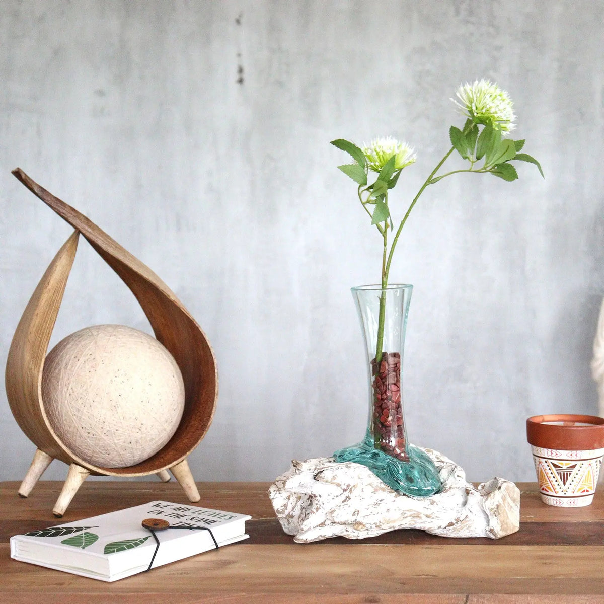Florero de vidrio fundido sobre base de madera blanqueada con flores artificiales sobre mesa de madera rústica