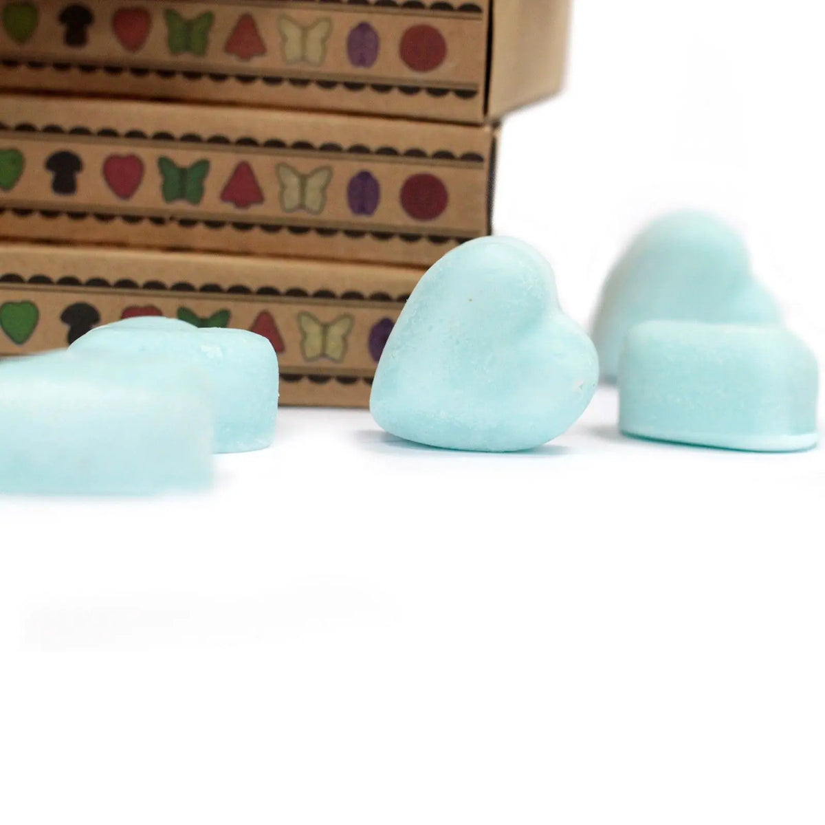 Ceras de soja azul claro en forma de corazón frente a cajas de cartón con dibujos de mariposas y corazones.