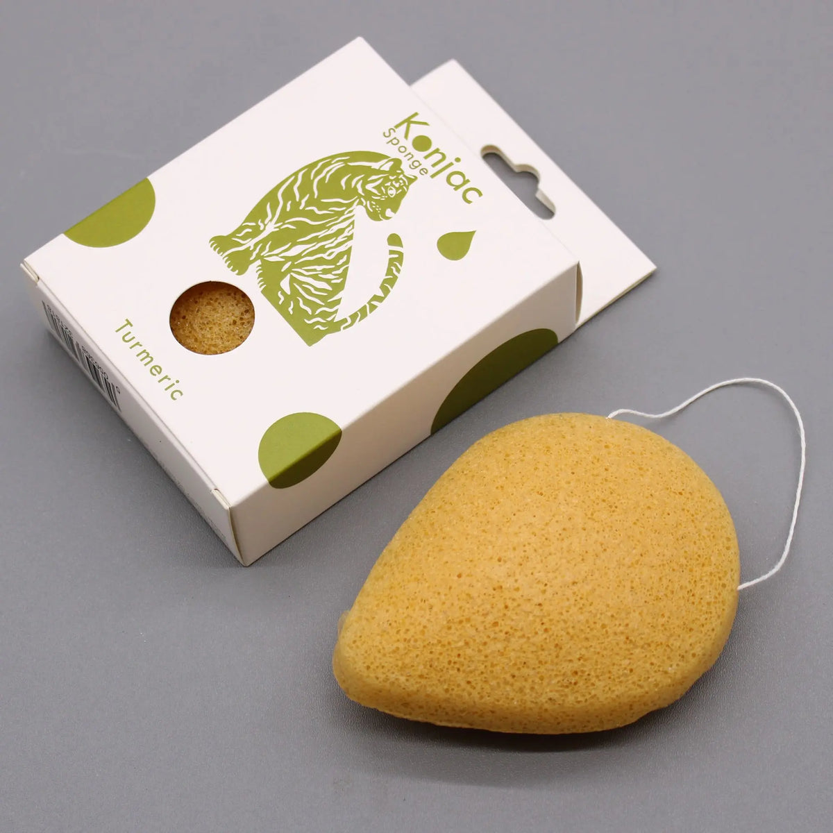 Esponja facial de konjac en forma de gota, color ocre, junto a su caja de cartón blanca con ilustración de un tigre.