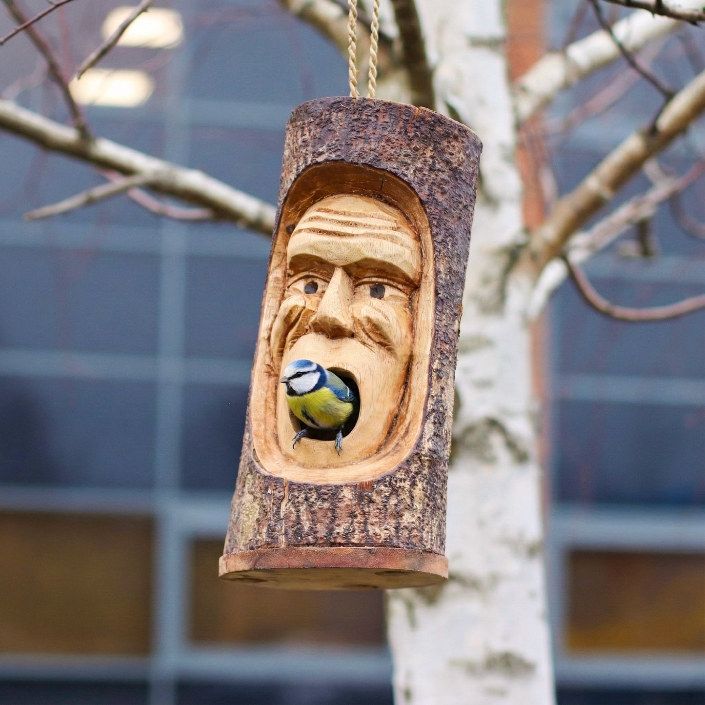 Comedero de pájaros de madera tallada en forma de cara, con color natural y diseño rústico, ideal para exteriores.