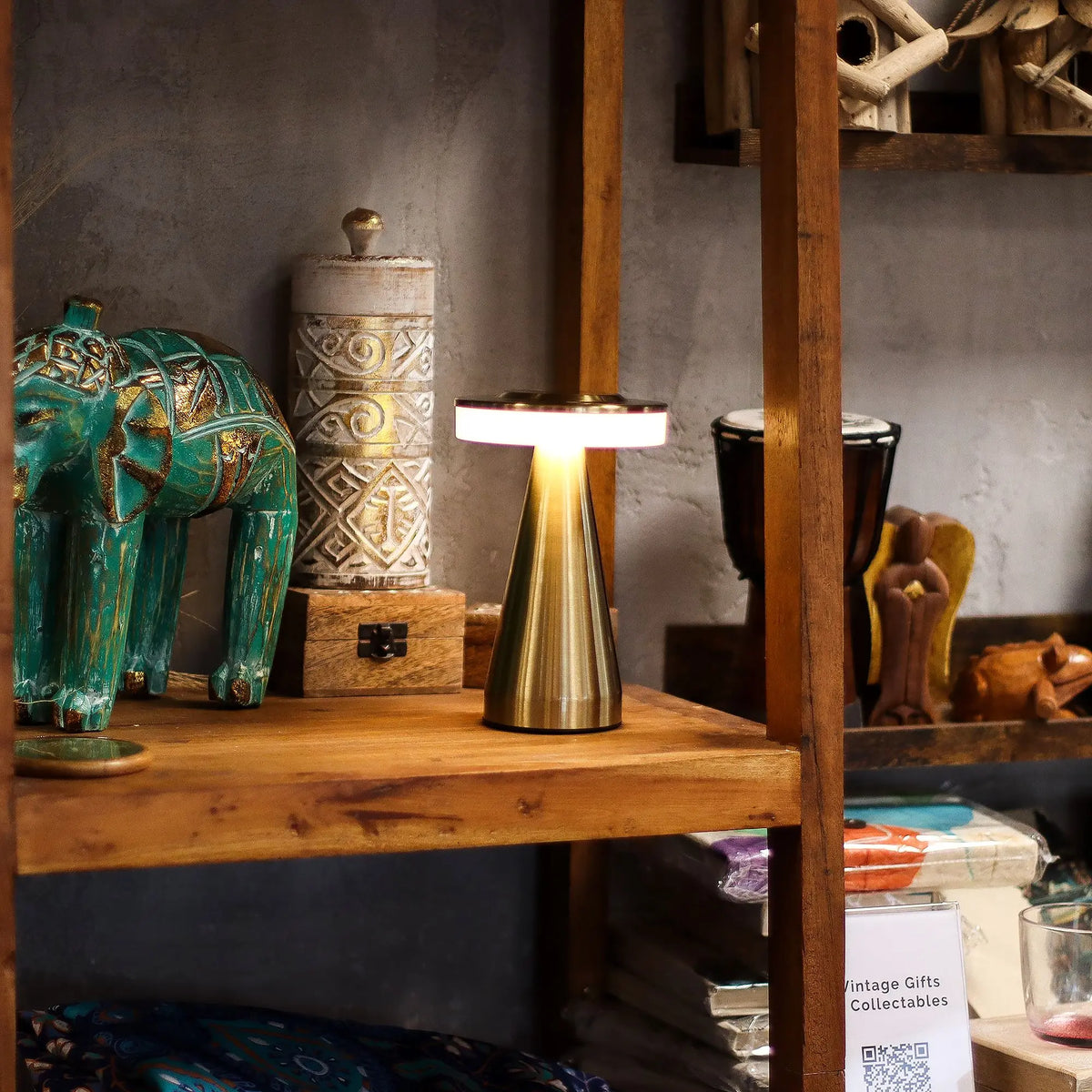 Lámpara de mesa táctil con tallo de cobre, diseño moderno, recargable y luz cálida sobre una estantería de madera